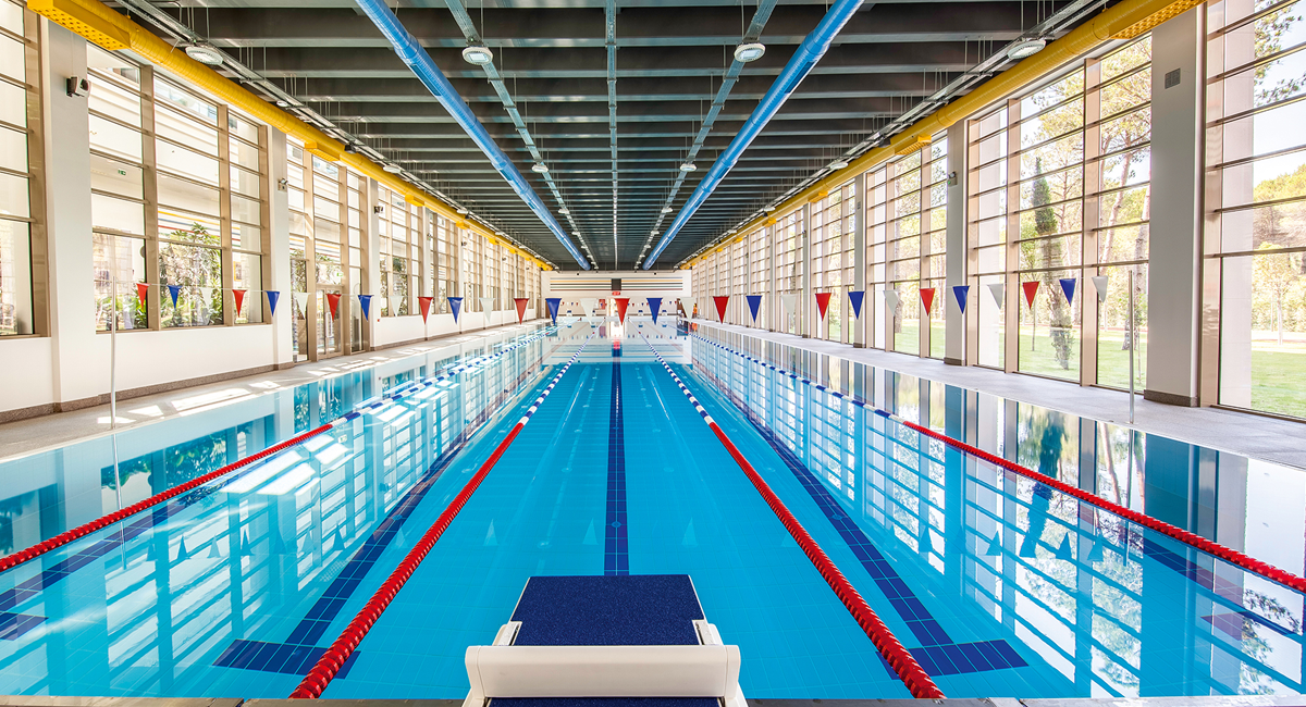 FINA standartlarına göre tasarlanmış, geniş cam cepheli ve kulvar çizgileri net şekilde görülen kapalı olimpik yüzme havuzu.